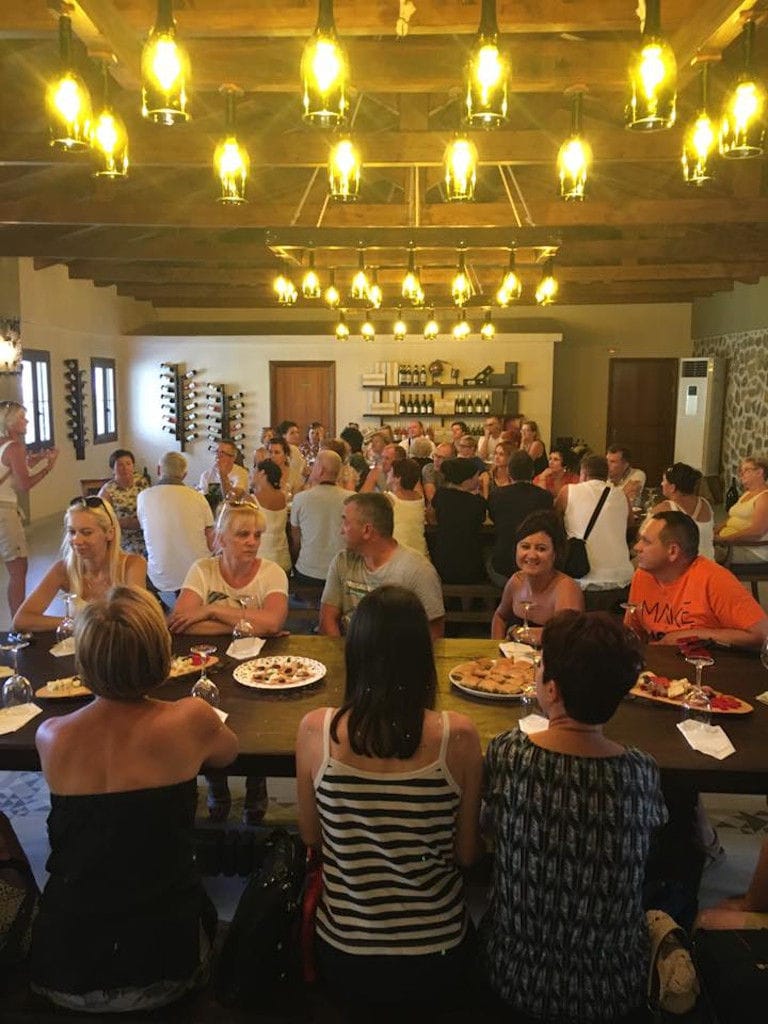 tourists eating and drinking at the wood tables with benches Ktima Karamitsos illuminated tasting room