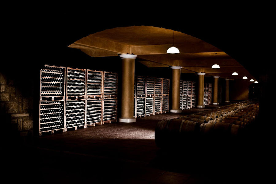 lying wooden barrels and stacked bottles on top of each other at illuminated 'Ktima Karipidis' cellar