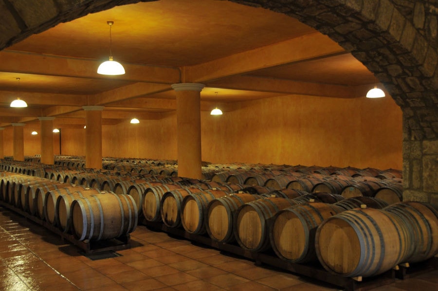 lying wooden barrels in a row at illuminated 'Ktima Karipidis' cellar with stone arcade