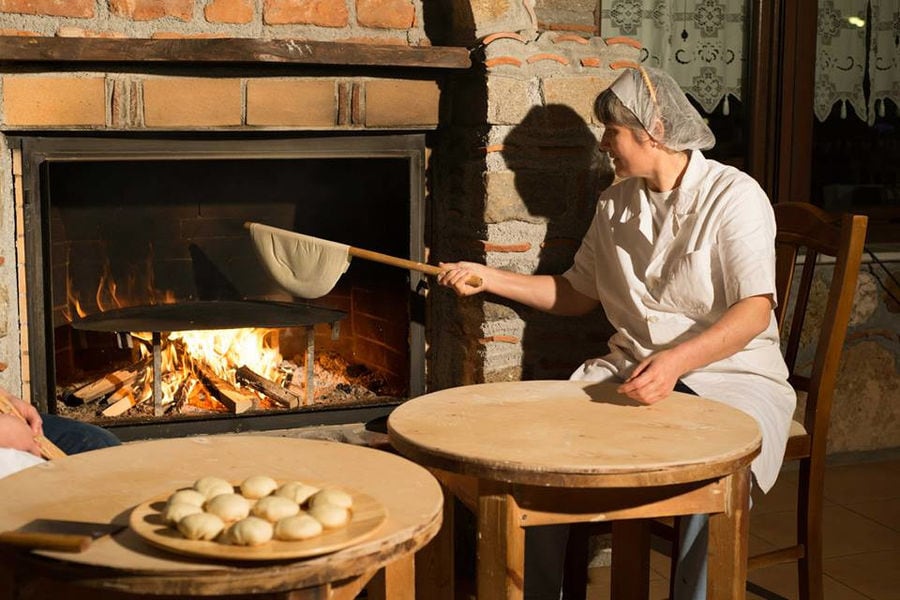 woman baking pitta bread into stone oven at Ktima Perek