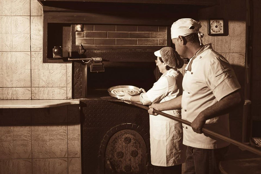 woman and man baking Greek spiral cheese pie into stone oven at Ktima Perek