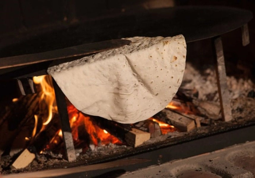 baking pitta bread on metallic support into stone oven at Ktima Perek