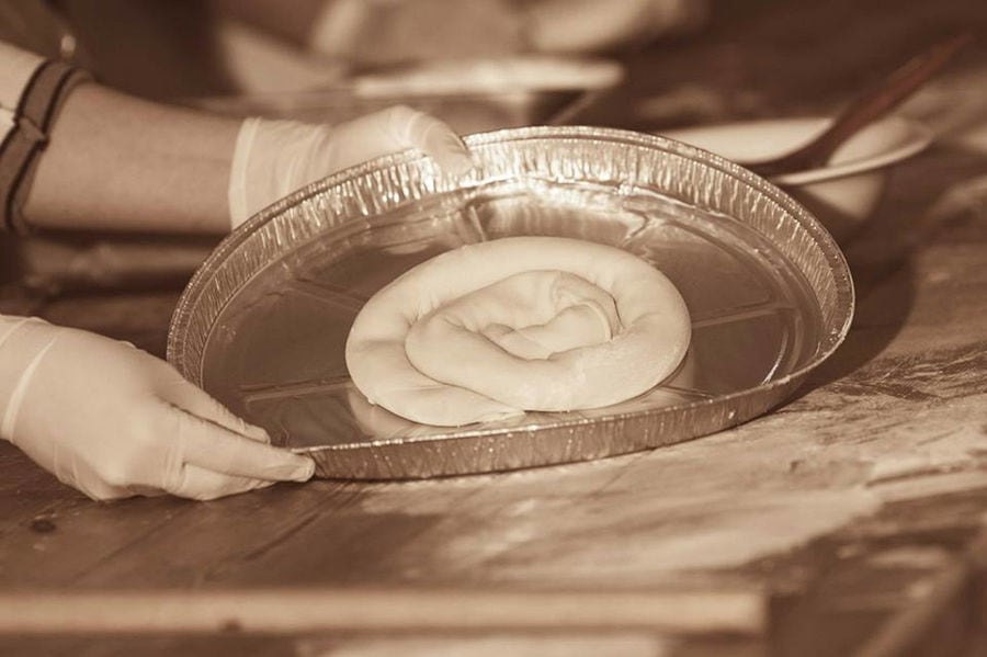 woman showing at the camera a bakery pan with Greek spiral cheese pie at Ktima Perek workshop