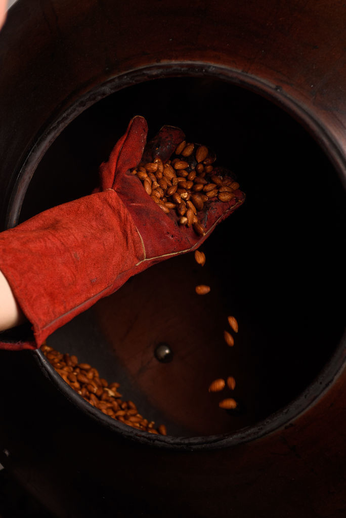 man with oven mitt holding roasted peanuts from the cauldron at Lazaris Distillery
