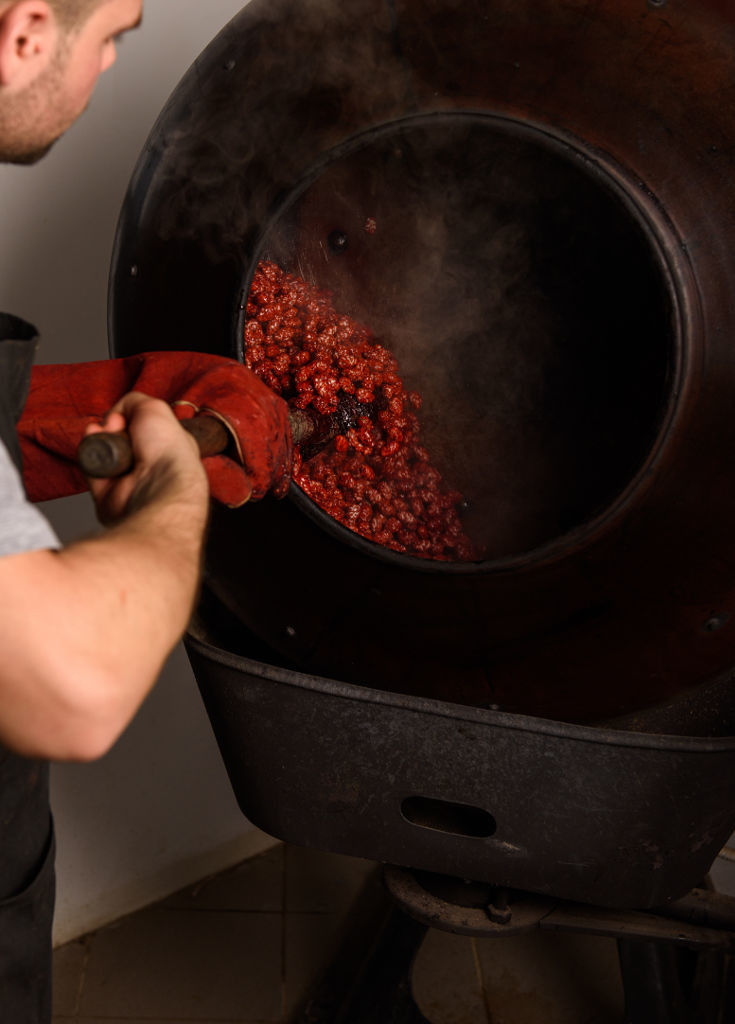 man with oven mitt using wood shovel to making Greek mandoles in cauldron at Lazaris Distillery