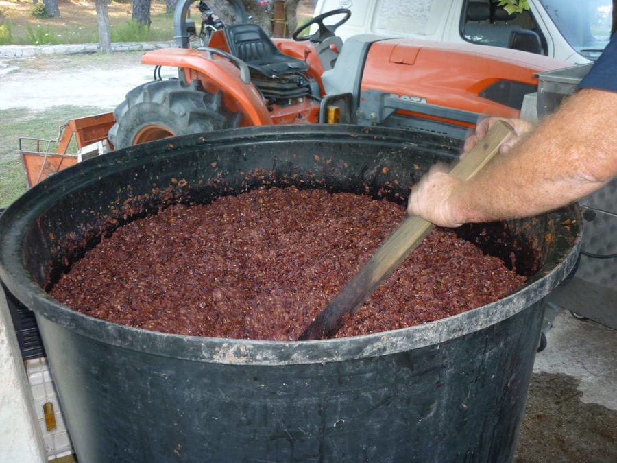 man mixing with a rod in a cauldron, the must 'pulp' of black grapes boiling at 'Lithies Organic Farm'