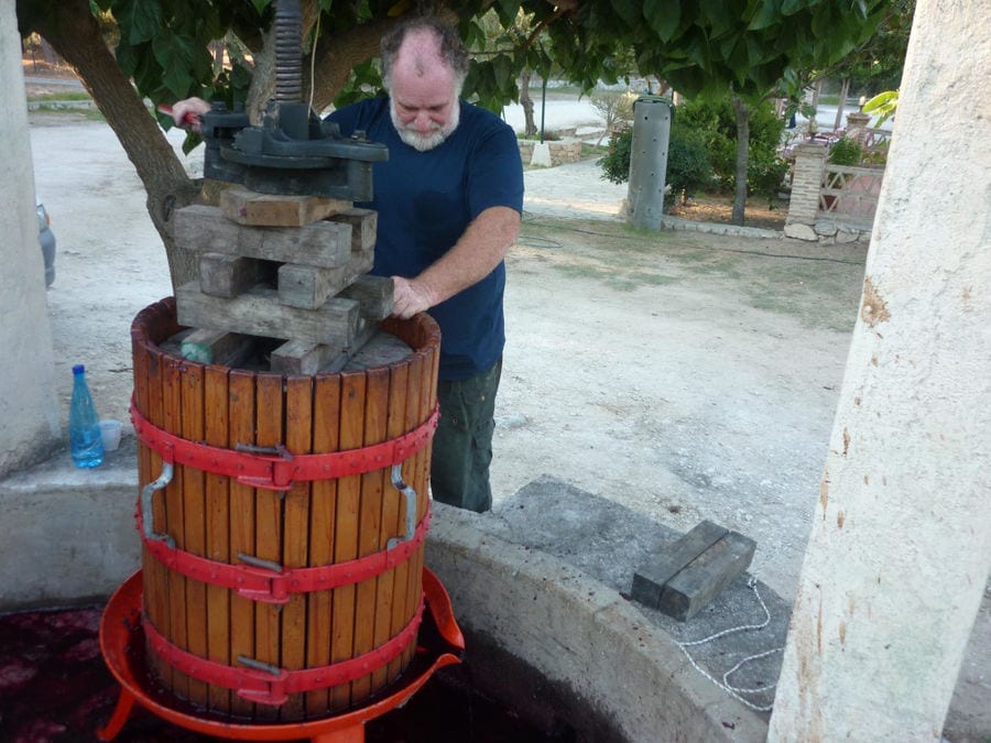 bearded man using manual old grape press outside 'Lithies Organic Farm'