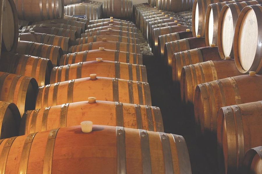 lying wine wood barrels someone on top of each other in a row at Domaine Dereskos cellar