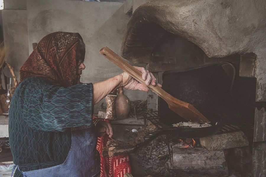 old woman baking hilopites pasta into stone oven at Maggiri facilities