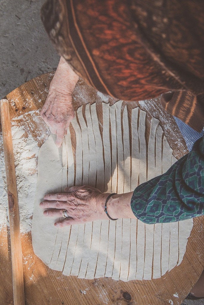 old woman using wood dough paddle to make dough at Maggiri facilities