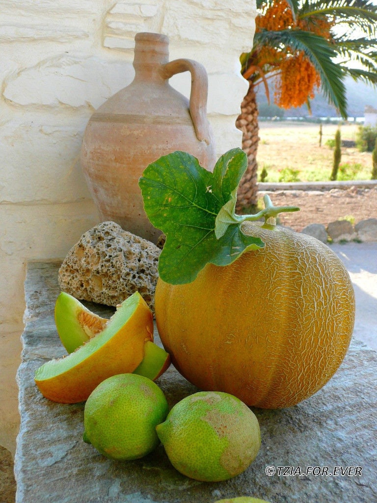 close-up of a melon and two slices of it and two lemons on stone surface at 'La Maison Vert Amande' with ceramic amphora in the background