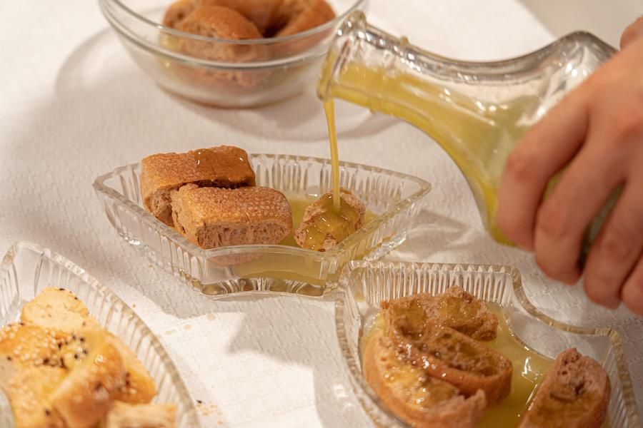 man pouring olive oil from the bottle on breadsticks in bowls at Politakis Olive Oil Mill