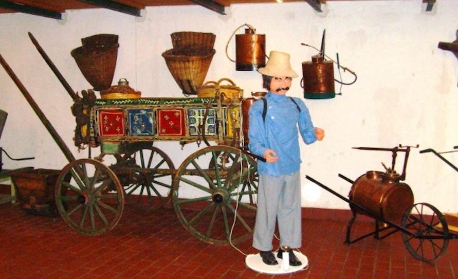 exhibit shows a man with sun hat and mustache and old hand painted wooden horse cart with four wheels in the background at Tzivani Bio Wines