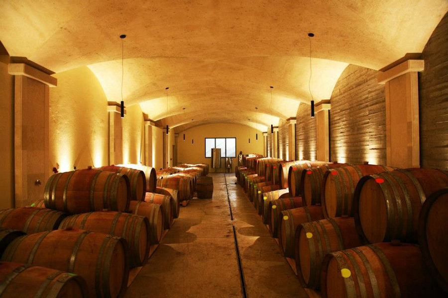 corridor of Manousakis Winery illuminated cellar and on the both sides wine wood barrels on top of each other in a row