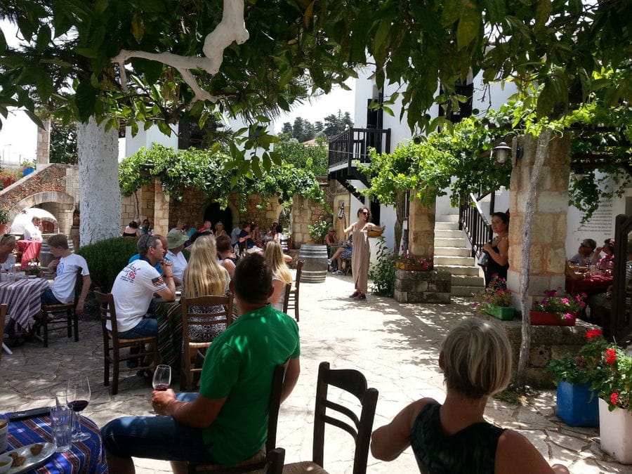 tourists sitting at the tables in the shade of the trees and listening to concert outside Manousakis Winery'