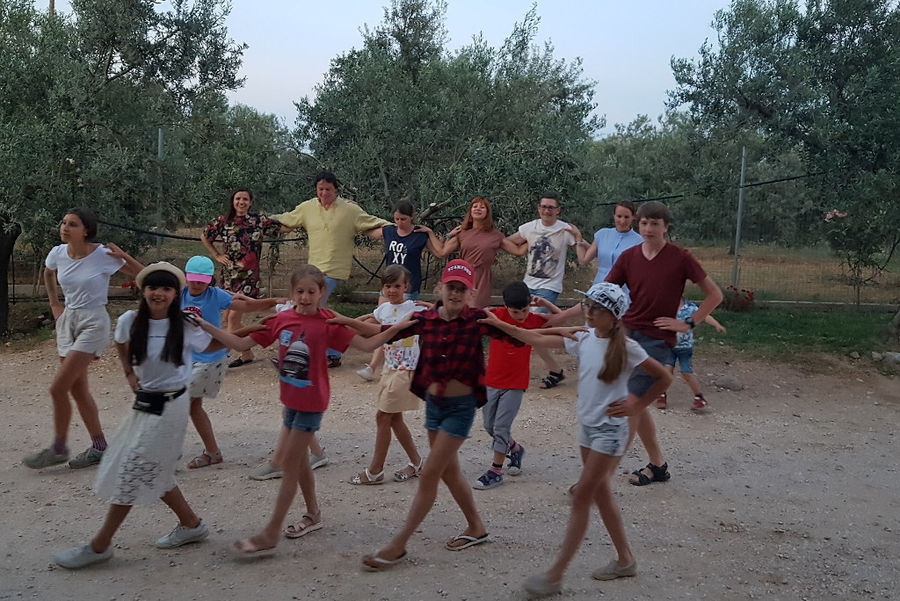 a group of children dancing outside at Melas Epidauros with olive trees in the background