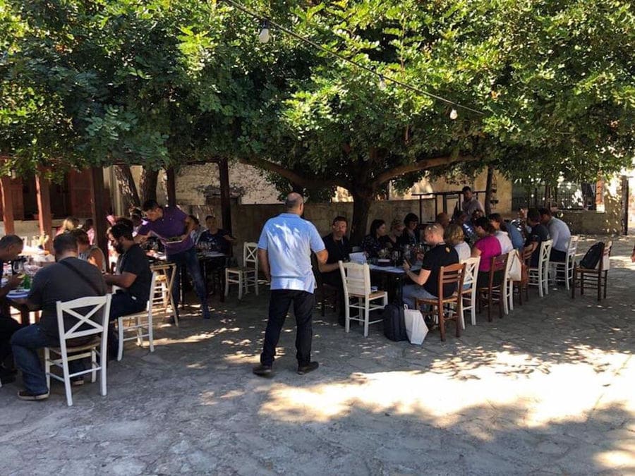 tourists listening to a guide at Minos - Miliarakis Winery outside and sitting in the shade of the tree