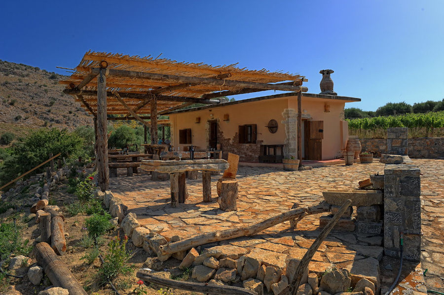 front view of Minos - Miliarakis Winery building with stone pavement and wooden tables