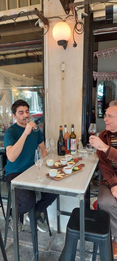 Two men enjoy a wine tasting session, with an array of delicacies in front of them.
