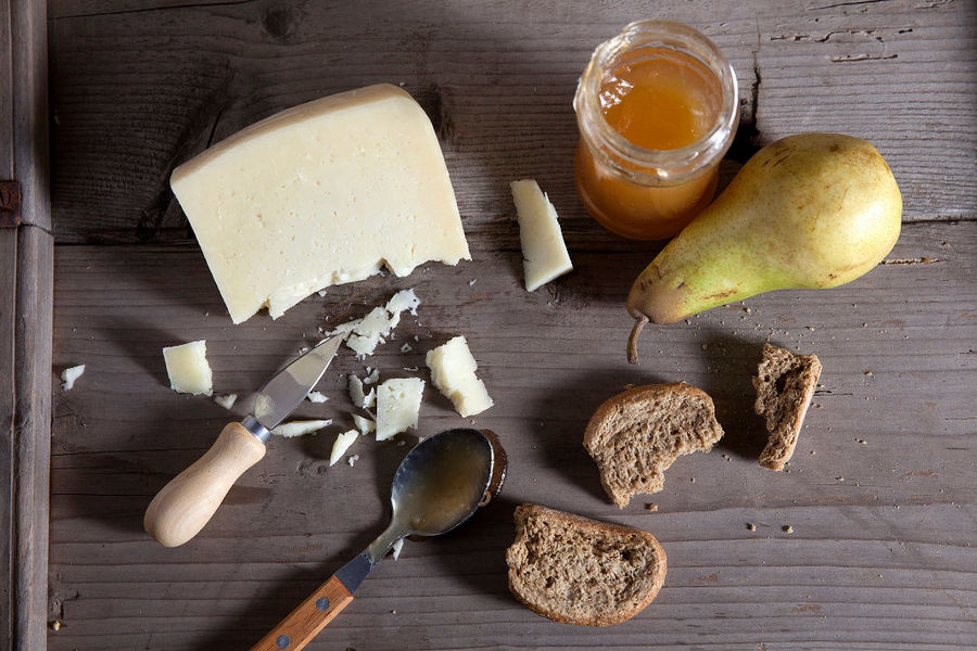 view from above of jar with honey and a piece of 'Mystakelli Dairy' white cheese and pieces of dry bread and a spoon on wood surface