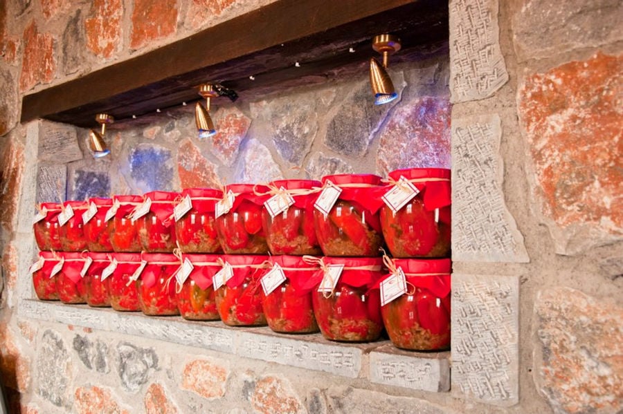 glass jars with Florina red peppers on the top of each other into a niche in a 'Naoumidis All Peppers' stone wall