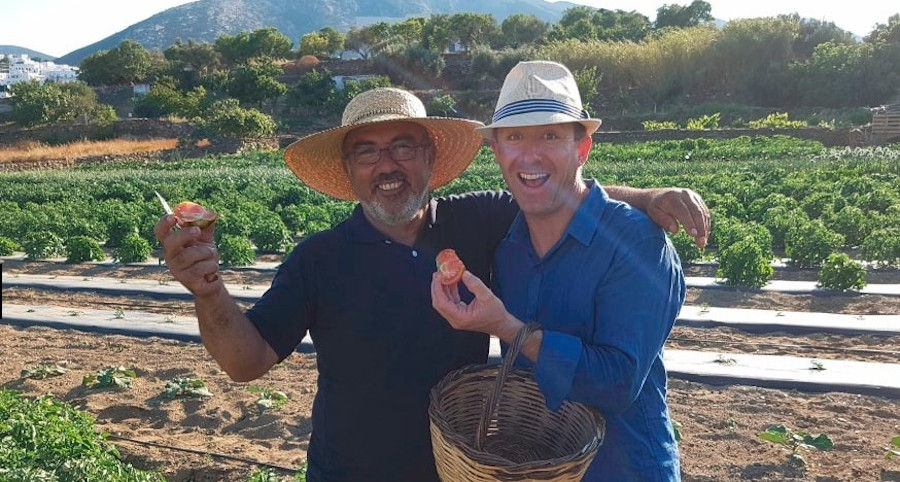 two tourits smiling happily at the camera at 'Narlis Farm' and holding a half of tomato each one