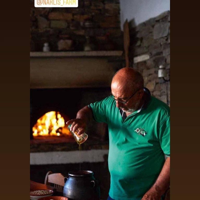 man putting olive oil in ceramic pot from a glass at 'Narlis Farm' kitchen with fireplace in the background