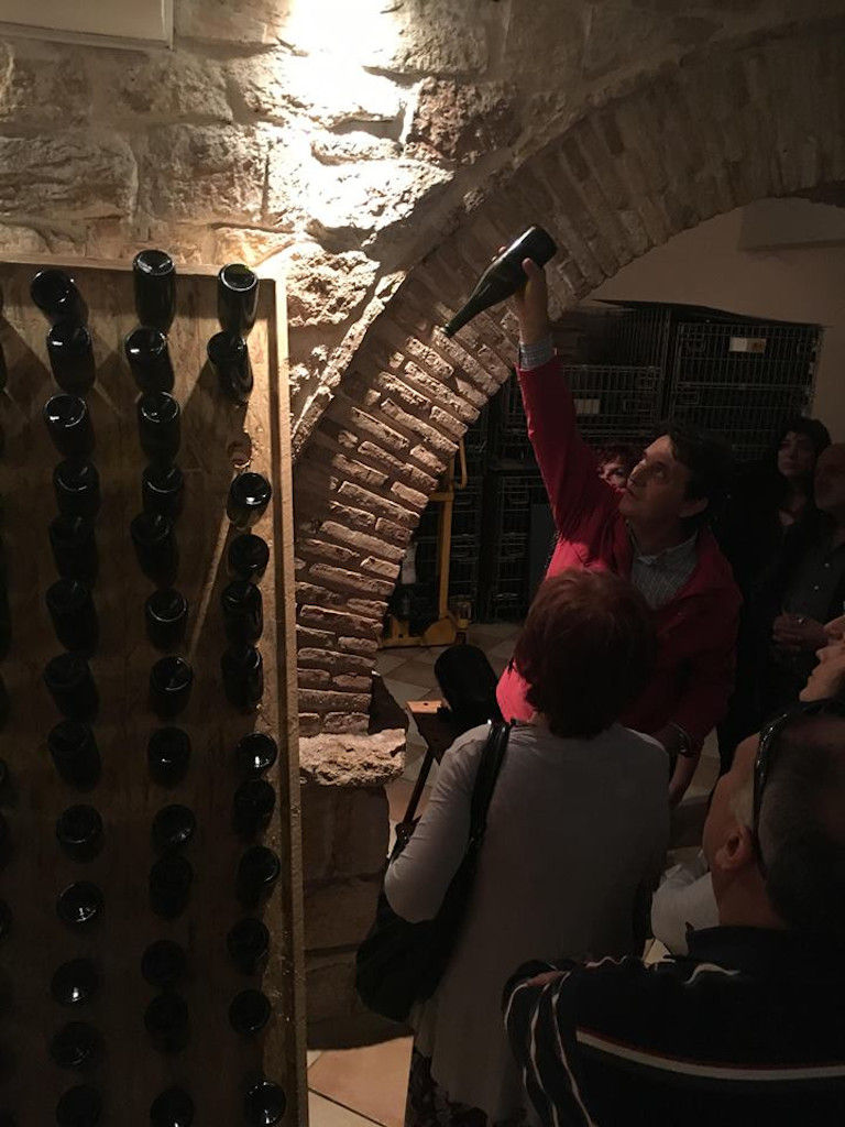 guide presenting tourists the Nikolou Winery stone cellar with wine bottles in the wall