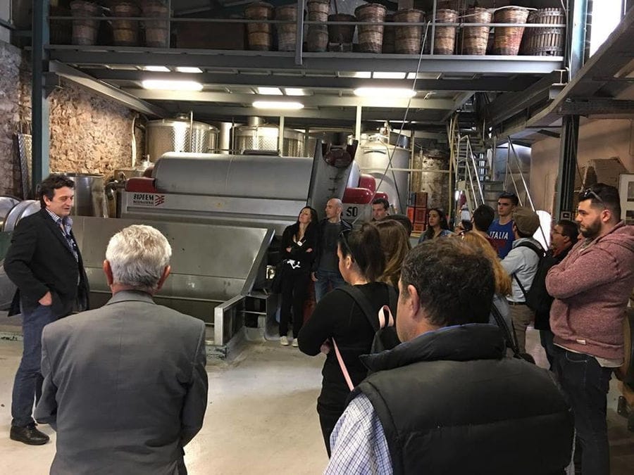 guide presenting tourists the Nikolou Winery plant in front of grape press machine
