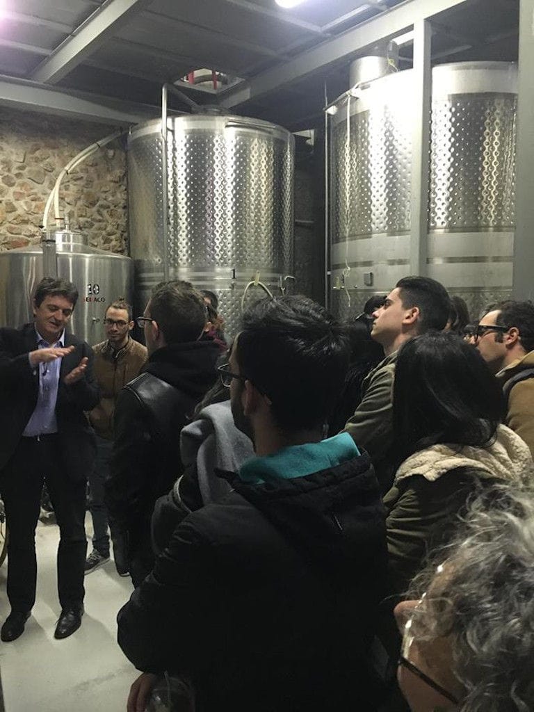 guide presenting tourists the Nikolou Winery plant in front of wine storage tanks