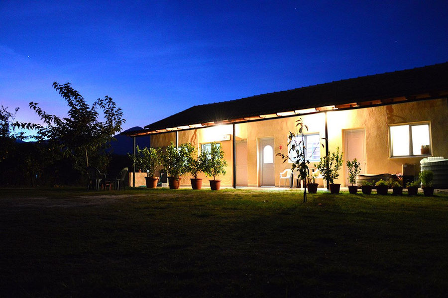 front view of 'Voskopoulos Handicraft' illuminated building by night surrounded by green lawn and trees