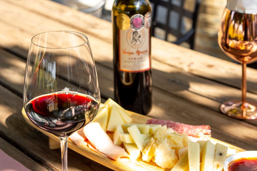 A glass of red wine, paired with a tantalizing selection of cheeses and ham.
