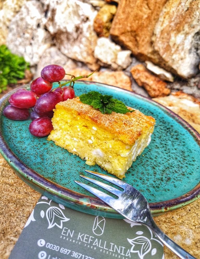 blue plate with piece of cheese pie, red grapes and a fork at En Kefallinia Organic Farm Restaurant