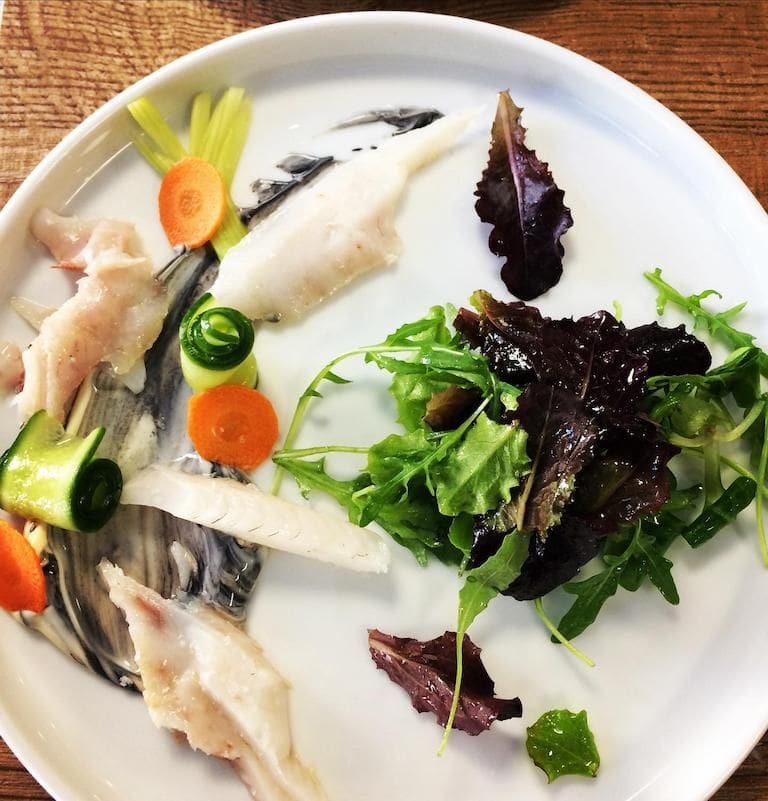 close-up of a plate with fish fillet, scallop, green salad and black sauce at Savor Nafplio