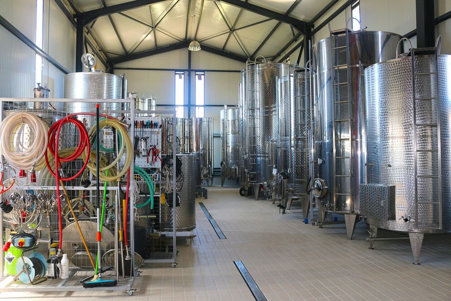 The distillation area of a winery is a large room with copper stills, barrels, and storage tanks. The air is filled with the aroma of alcohol as workers monitor the process of converting grape must into high-proof spirits.