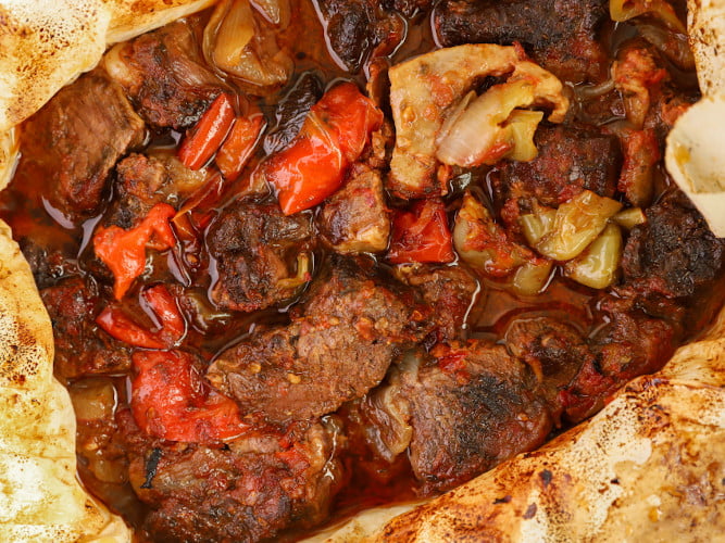 Cooked pieces of ‘Provatina’, female lamb meat with peppers, tomatoes and oil in oven