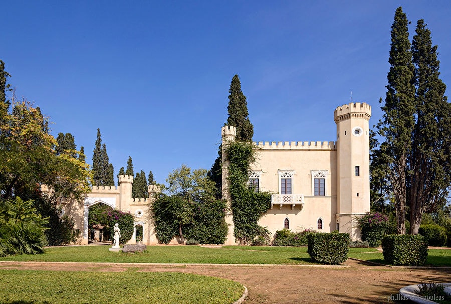 tall towers part of Pyrgos Vasilissis winery surrounded by trees, green lawn and garden