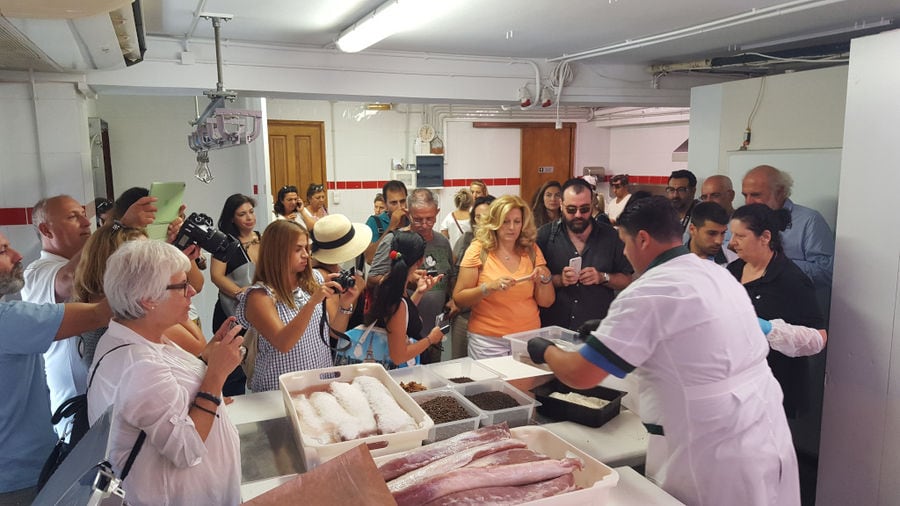 tourists observing and taking pictures of a man processing meat at 'Roussounelos Meat Market'