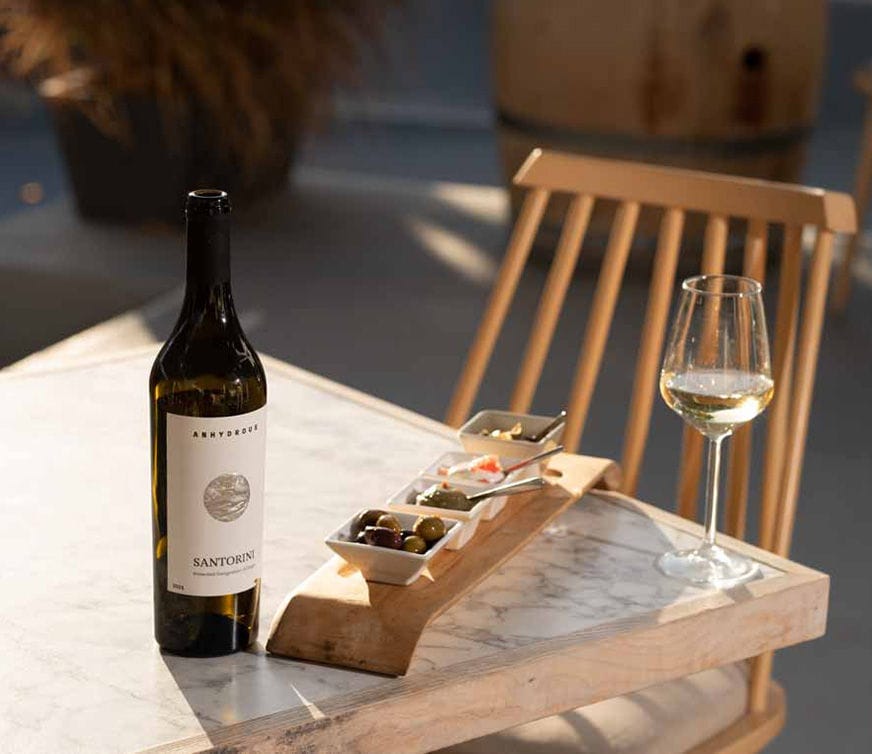 A tastefully arranged table with white wine bottle, glass, and a delectable platter showcasing a variety of delicacies for a delightful wine tasting experience.