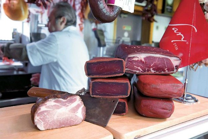 pieces of processed meat and cleaver on wooden counter with a man in the background at 'Sary'