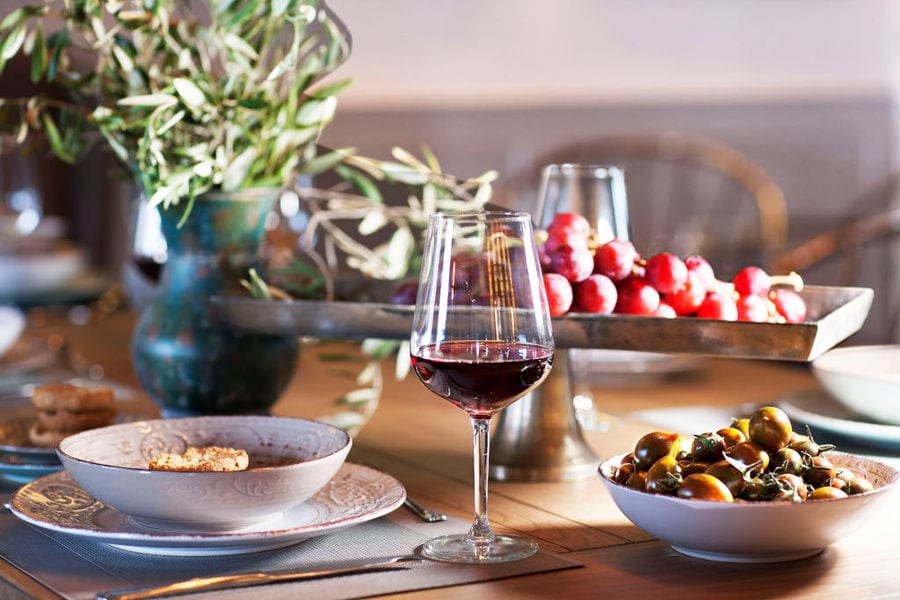 a glass of red wine and green olives and a vase with olive branches on the table of 'Semeli Estate'