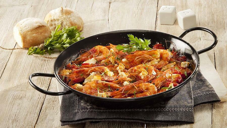 Cooked Greek Saganaki means fried shrimps with white cheese in a small pan with two handles