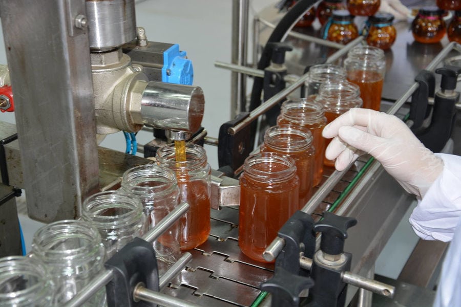 close-up of honey filling machine working and a woman placing the jars at 'Si-Mel Honey Toplou' plant