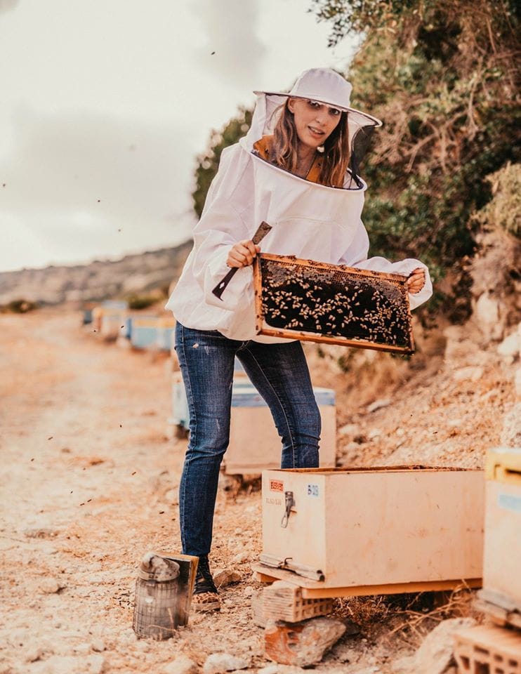 woman beekeeper holding honeycomb panel and a shovel and showing at the camera at 'Si-Mel Honey Toplou'