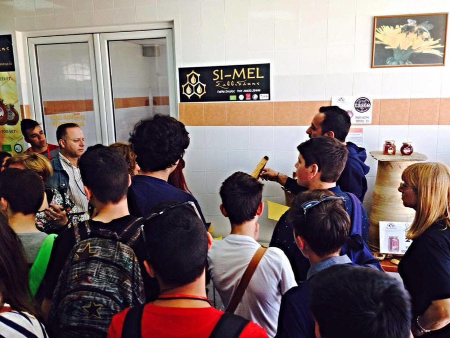 a group of young tourists listening to a man giving a tour at 'Si-Mel Honey Toplou' plant