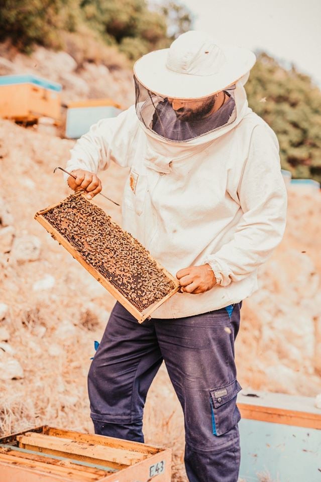 man beekeeper holding honeycomb panel and a shovel and showing at the camera at 'Si-Mel Honey Toplou'