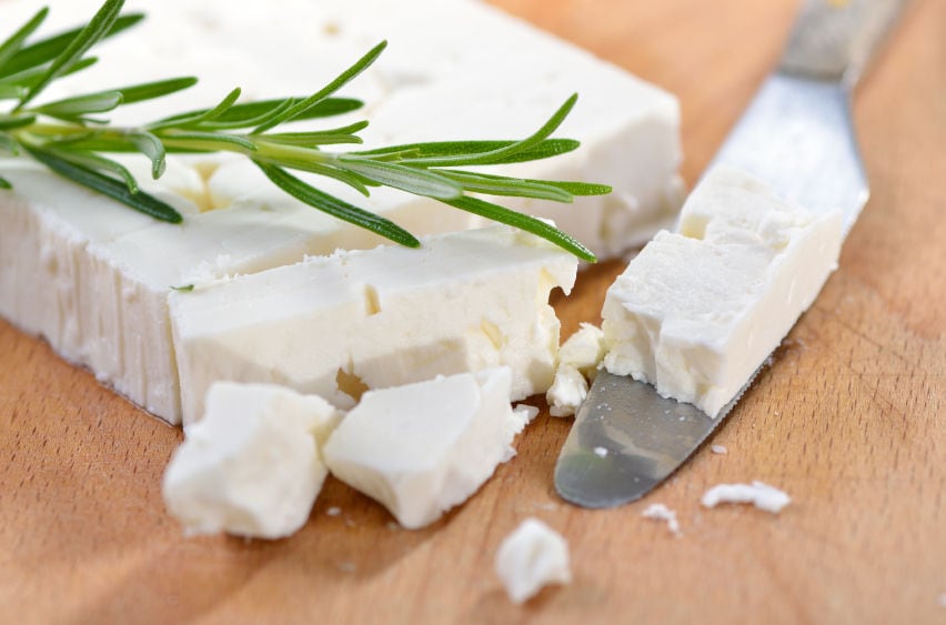 pieces of 'feta' cheese from Siafarikas Dairy on wood surface and on a knife and bushe of fresh rosemary