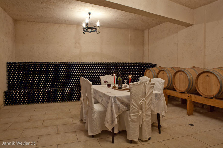 table with chairs, wine barrels and stacked bottles storaged in the wall at 'Stilianou Winery' cellar
