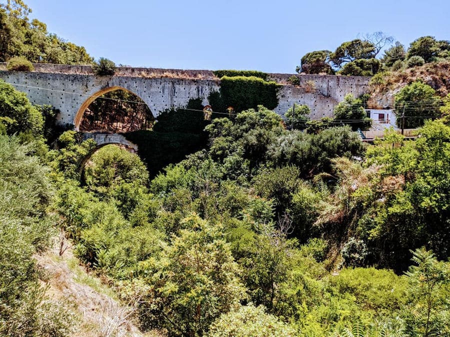 old stone bridge surrounded by trees and bushes of green plants in 'Stilianou Winery' area