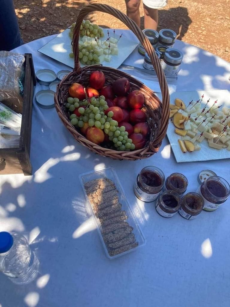 view from above of a basket with apples and grapes, jars with fig marmalade, pieces of cheese, all set on a white tablecloth at Figland